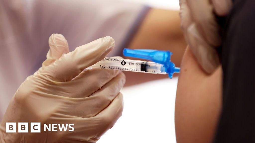 A close-up photo of a gloved hand injecting a vaccine into a person's arm.